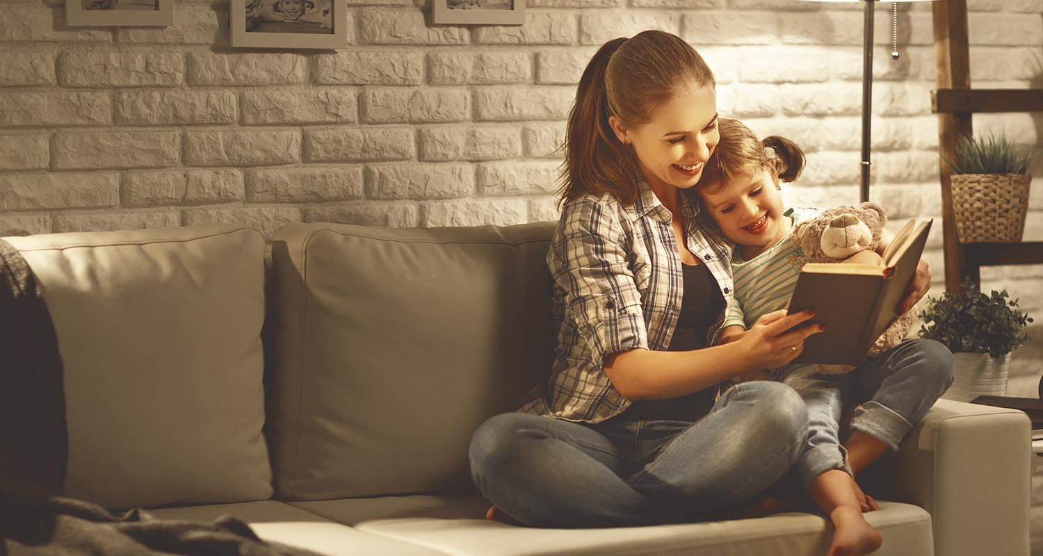 Una madre y su hija en el sofá de su casa con un libro