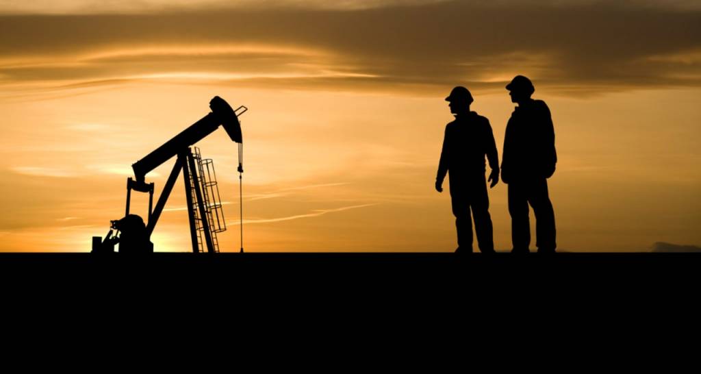 Two men next to a pump jack at dusk