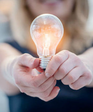 Detail of hands holding a lit light bulb