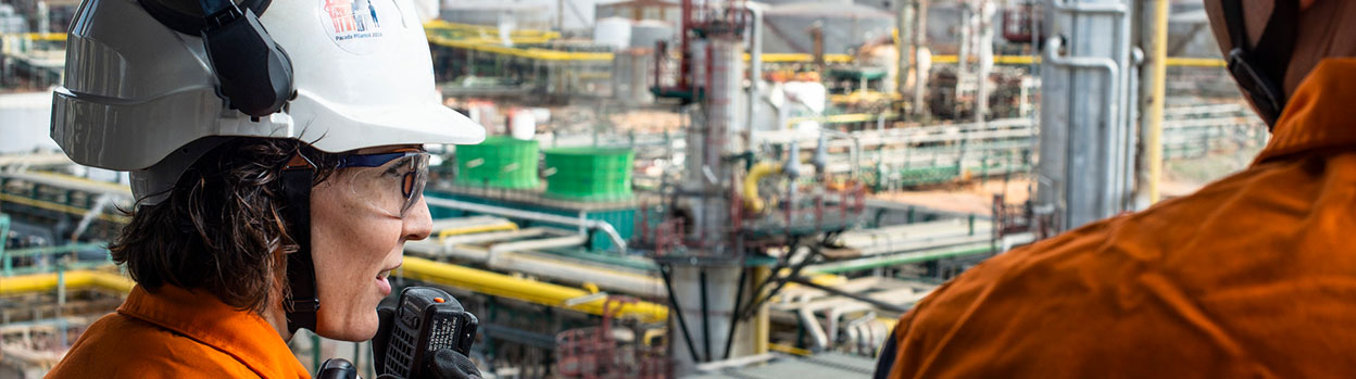 Operators working at a refinery, one of them talking on a walkie talkie